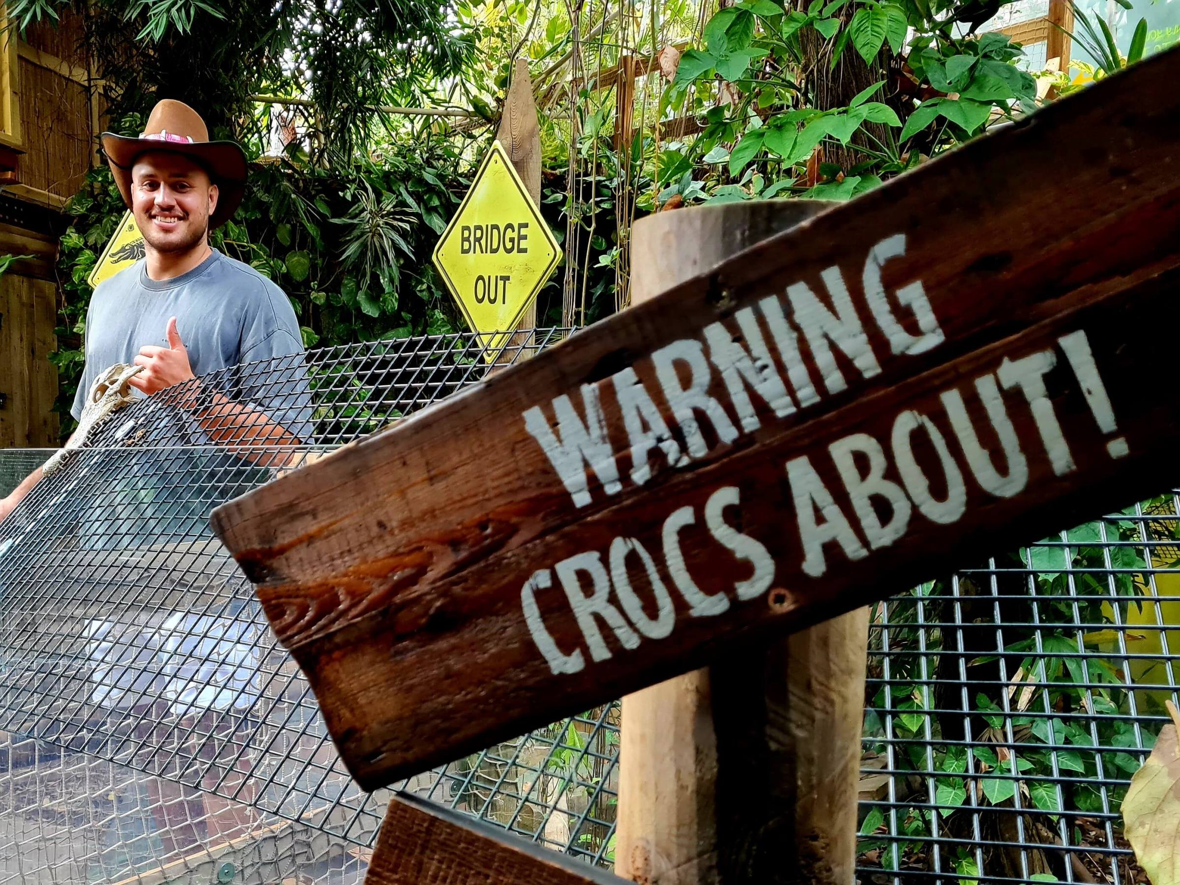 a person standing on a bridge behind a WARNING! CROCS ABOUT sign