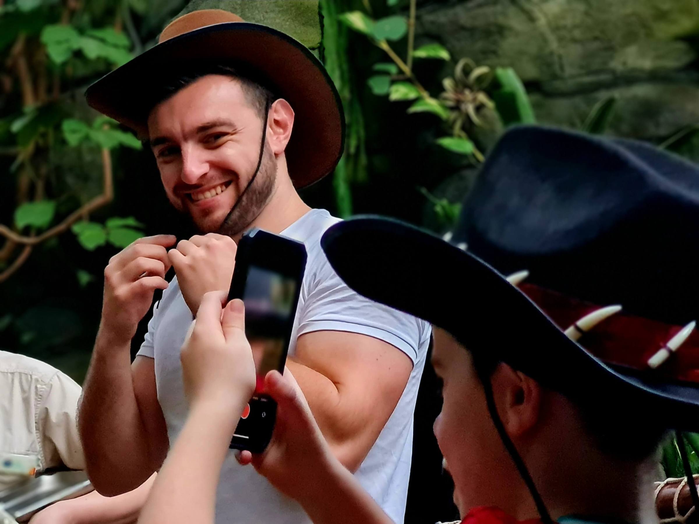 a man wearing an Australian hat, having his photo taken by a young biy with a mobile phone