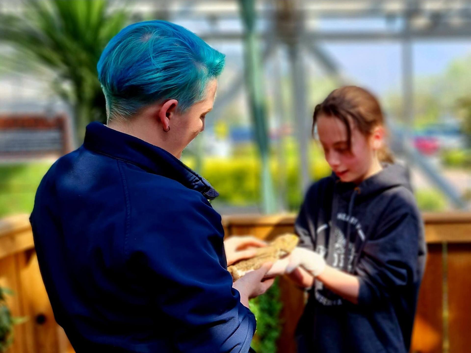 a zookeeper standing next to a child holdoing a bearded dragon