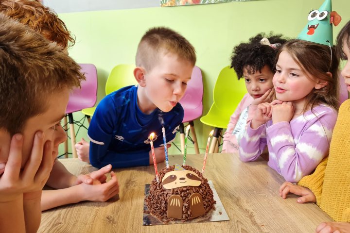 a group of children sitting at a table with a birthday cake