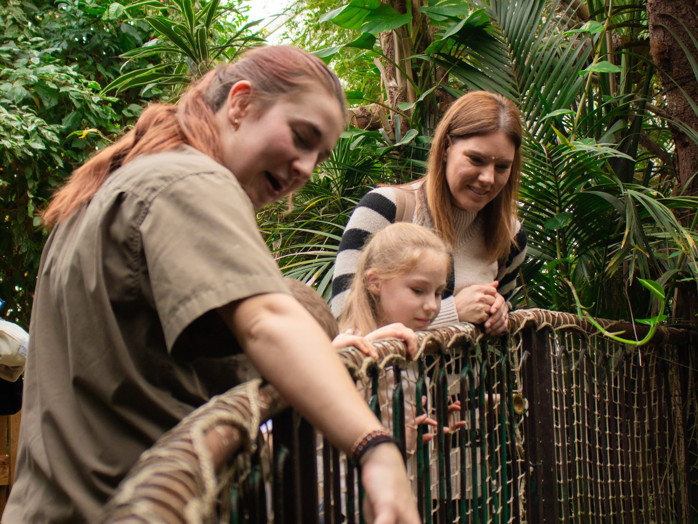 Two women and a child looking over a railing surrounded by lush greenery, pointing at something.