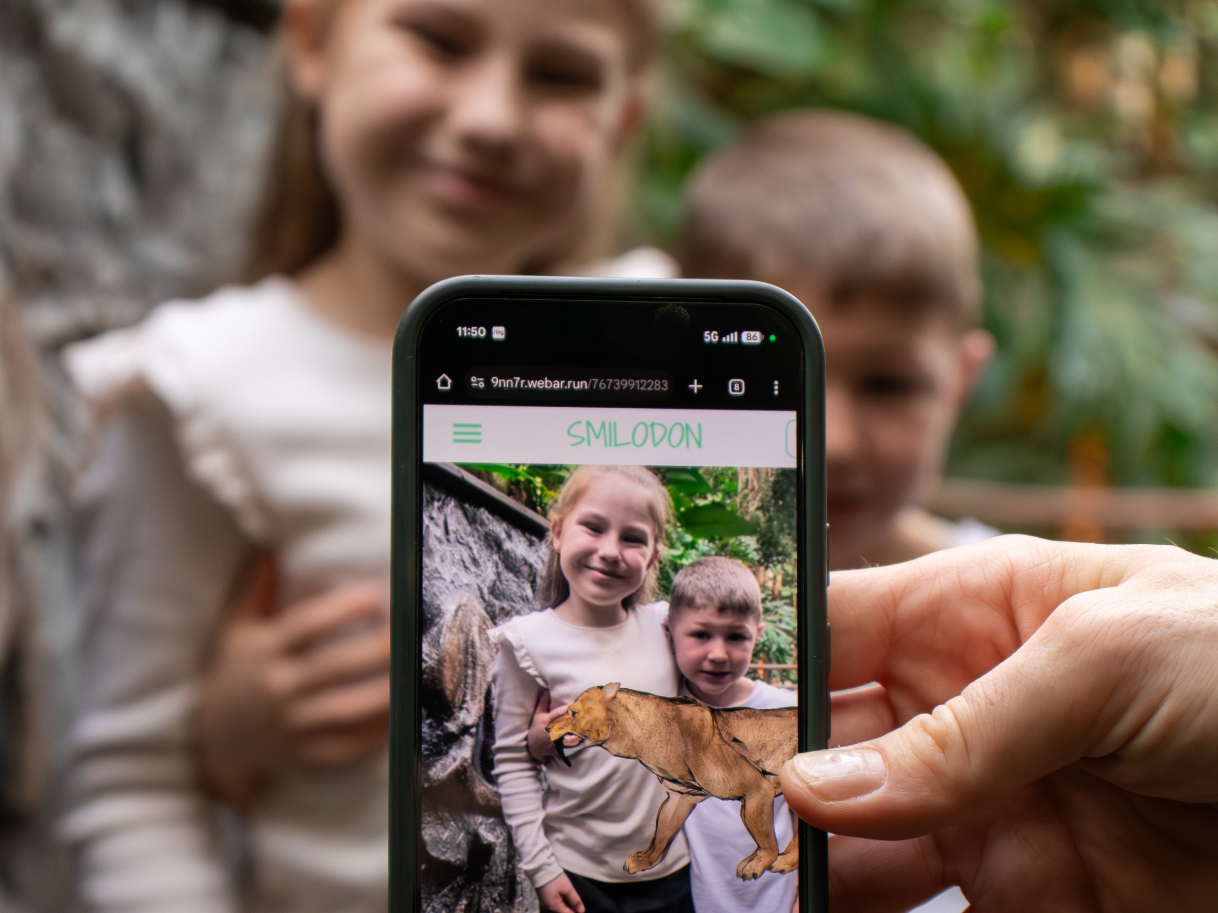 Phone showing children with a Smilodon image overlay, held in front of blurred background of the actual children.
