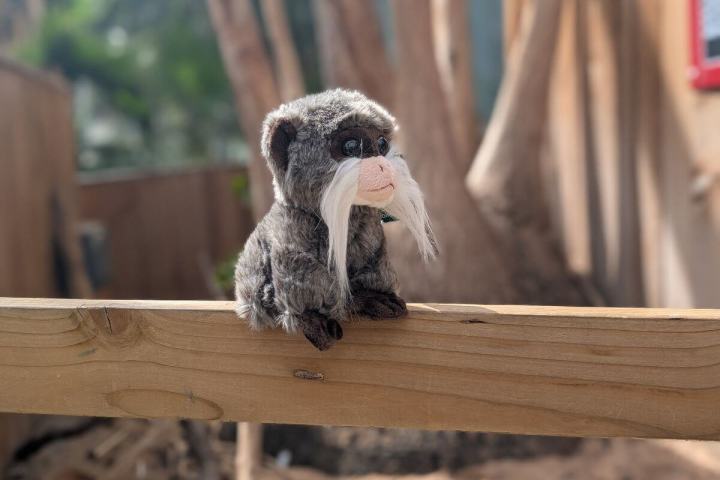 Plush monkey with white mustache on wooden rail outdoors.
