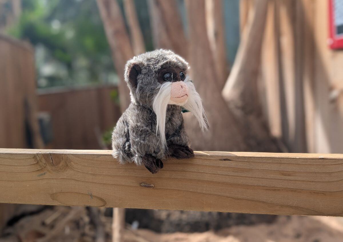 Plush monkey with white mustache on wooden rail outdoors.
