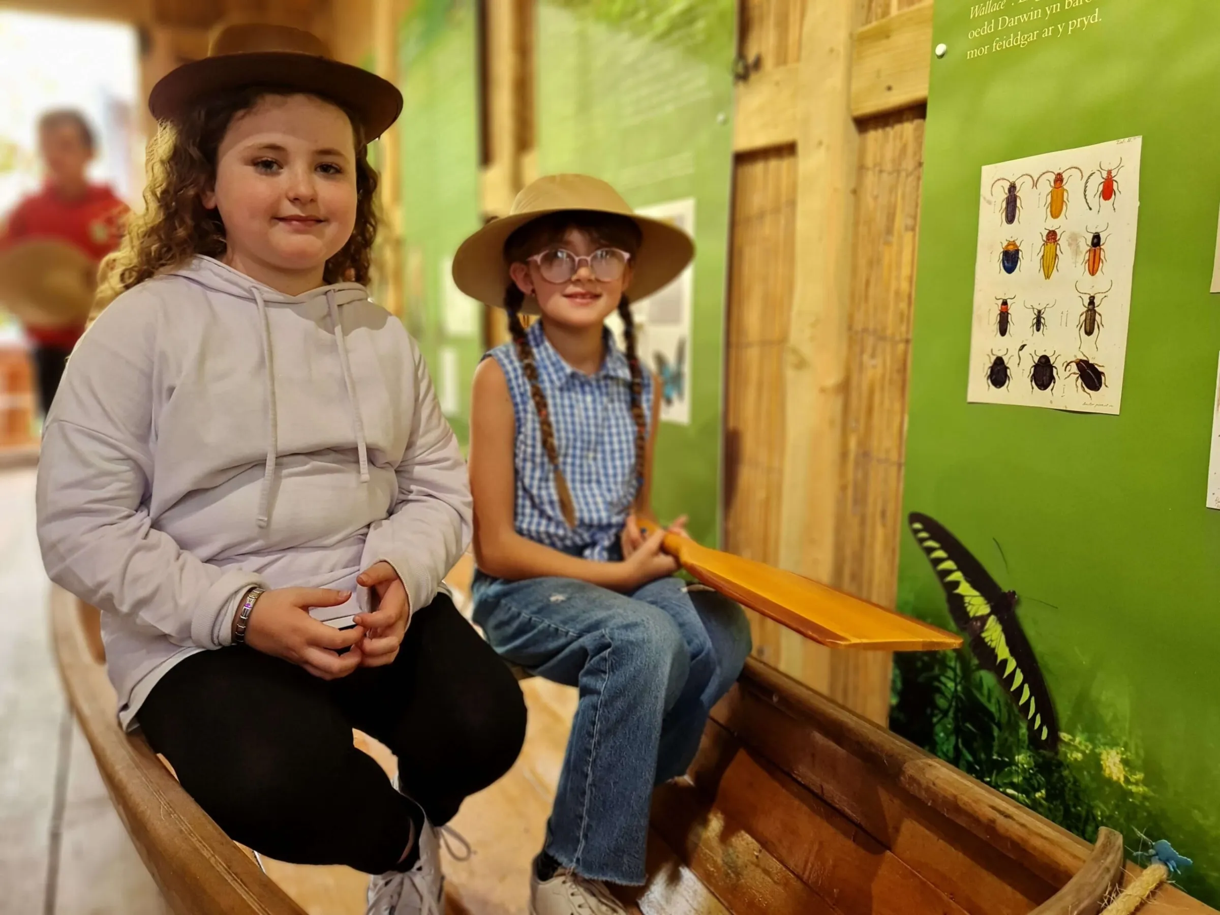 two children sitting on a bench wearing explorer hats