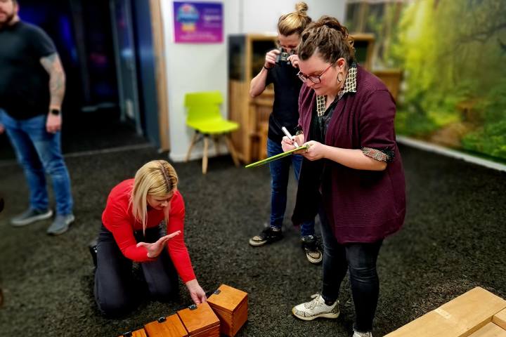A woman writing on a board and a woman on the floor looking at a line of wooden boxes