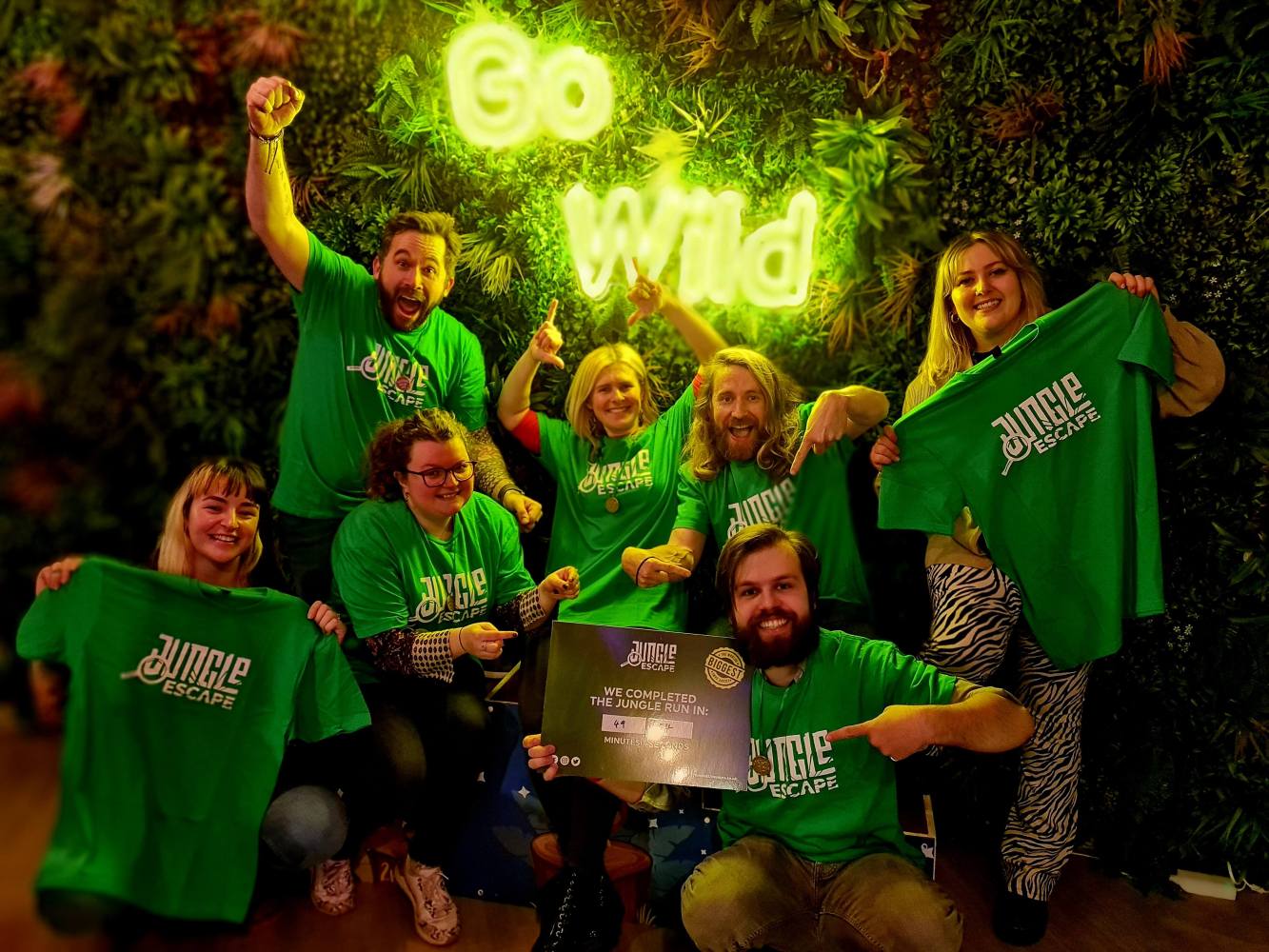a group of people posing for the camera holding green Jungle Escape t-shirts