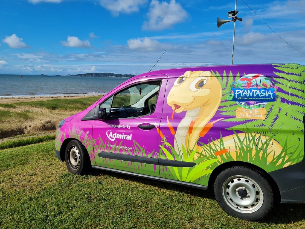 a purple branded van parked in a grassy field by the sea