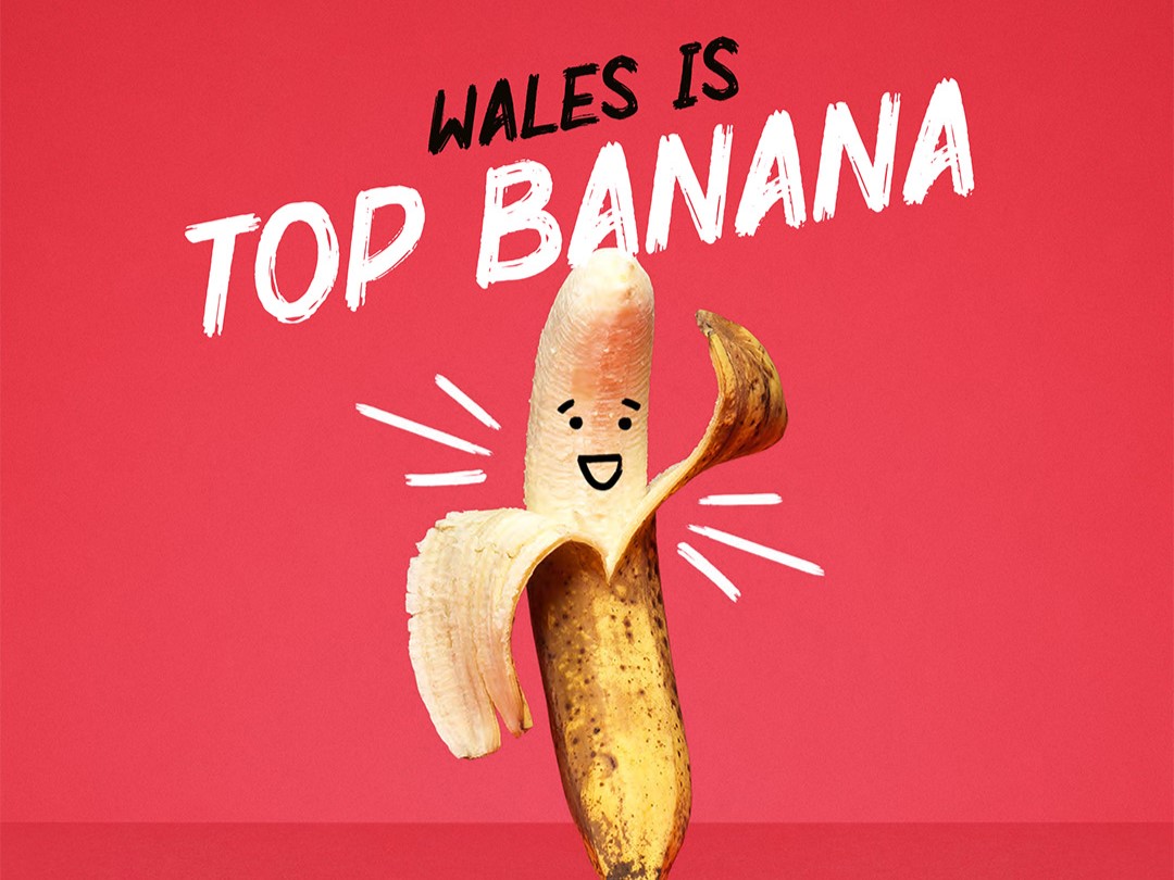 A half peeled banana with a face on a red background with WALES IS TOP BANANA written above