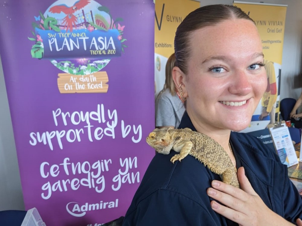 A zookeeper with a bearded dragon on her sholder posing for the camera