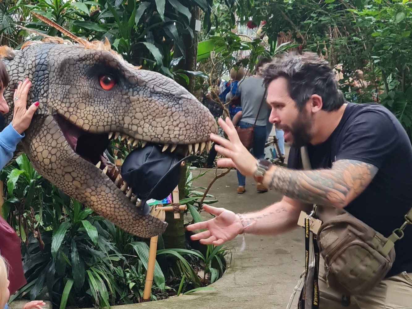 a man holding the head of a giant dinosaur, with his hat in the dinosaurs mouth!