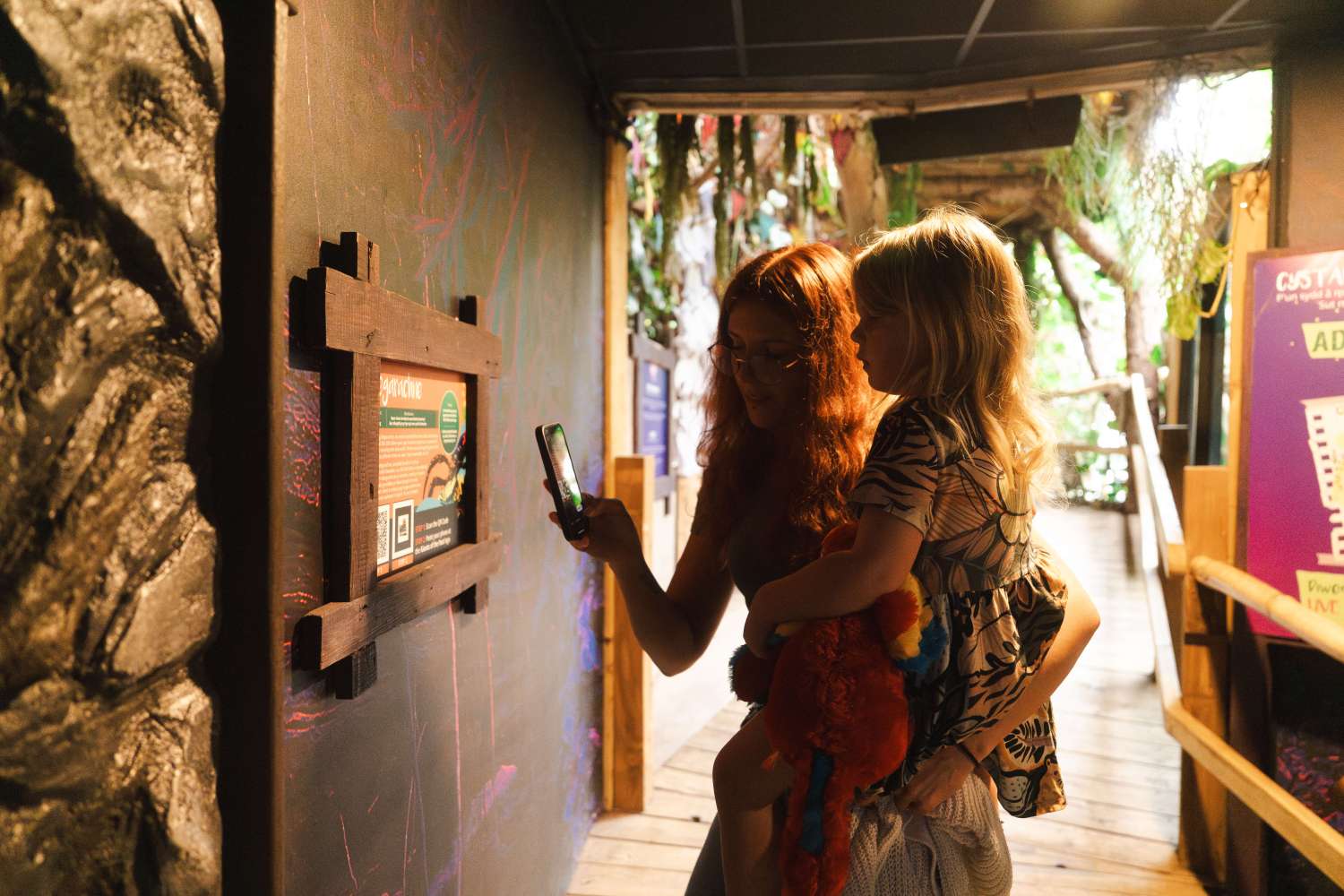 A mum and daughter holding a mobile phone to enjoy the AR experience of the Giants of the Past installation at Plantasia Tropical Zoo 