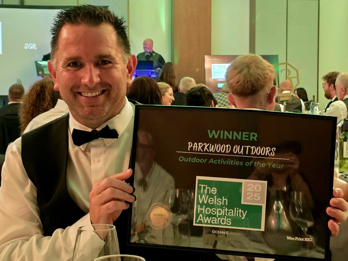 Person holding a framed award plaque for 'Outdoor Activities of the Year' at a formal event.