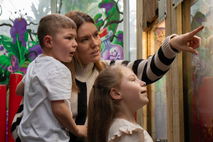 Woman with two children looking and pointing at an exhibit or window display.