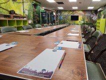 Meeting room with long wooden table, chairs, notepads, and pens, decorated with jungle-themed wall art.