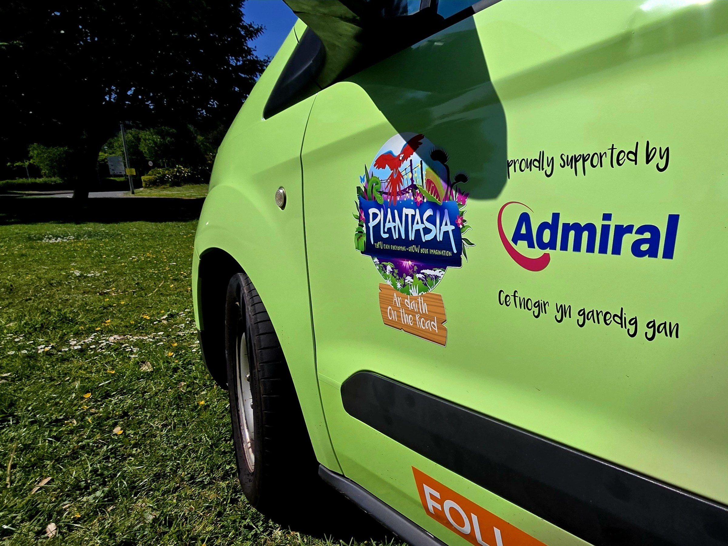 Side view of a green vehicle with Plantasia and Admiral logos parked on grass.