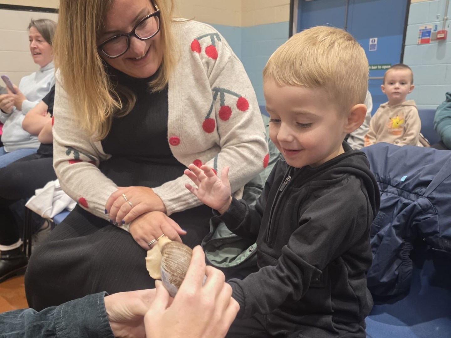 Adult looking at a child smiling while holding an African land snail in an indoor setting.