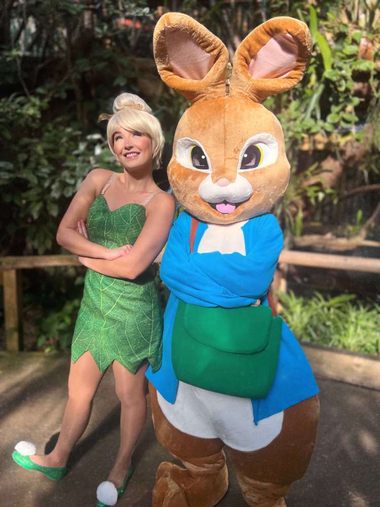 A female fairy in green dress poses with person in large bunny costume inside Plantasia Tropical Zoo.