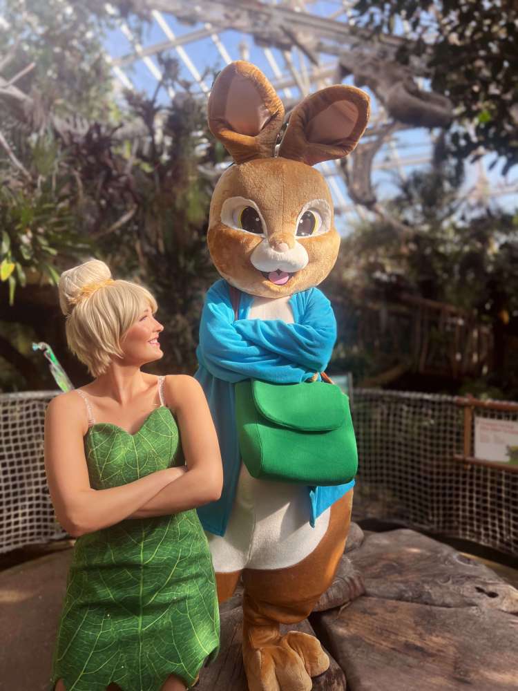 A female fairy in a green dress with a costumed rabbit character inside the greenhouse at Plantasia Tropical Zoo.