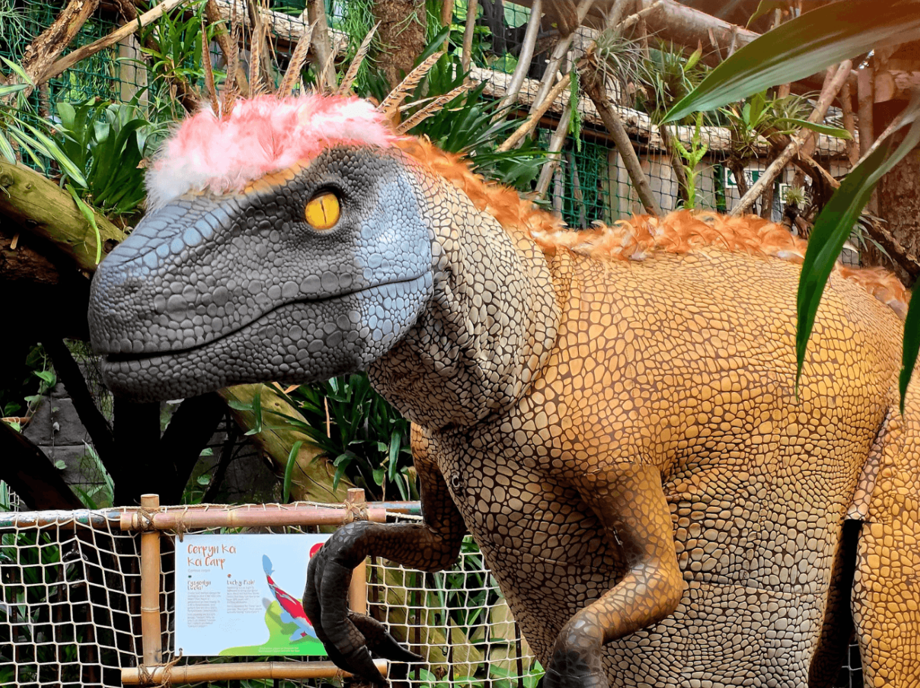 Dinosaur statue with pink wig in a tropical setting.